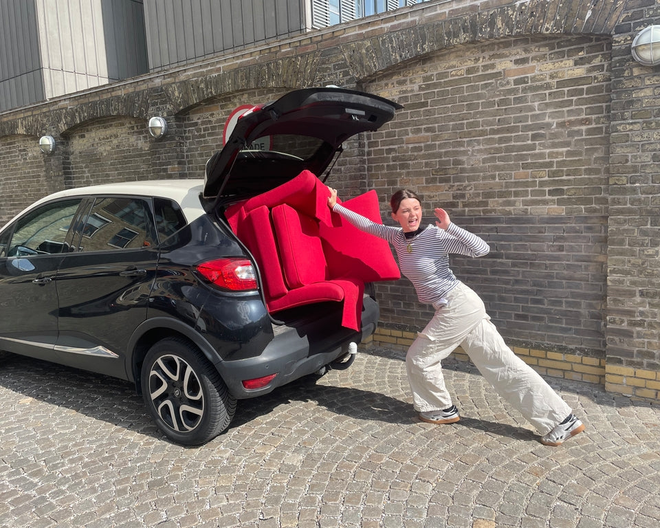 Pige der prøver at skubbe en lænestol fra genbrug ind i bagagerummet på en lille bil